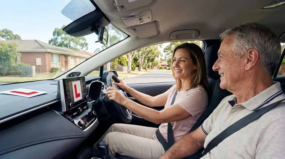 refresher driving lessons Melbourne – confident woman regaining driving skills with supportive instructor in automatic Toyota Corolla